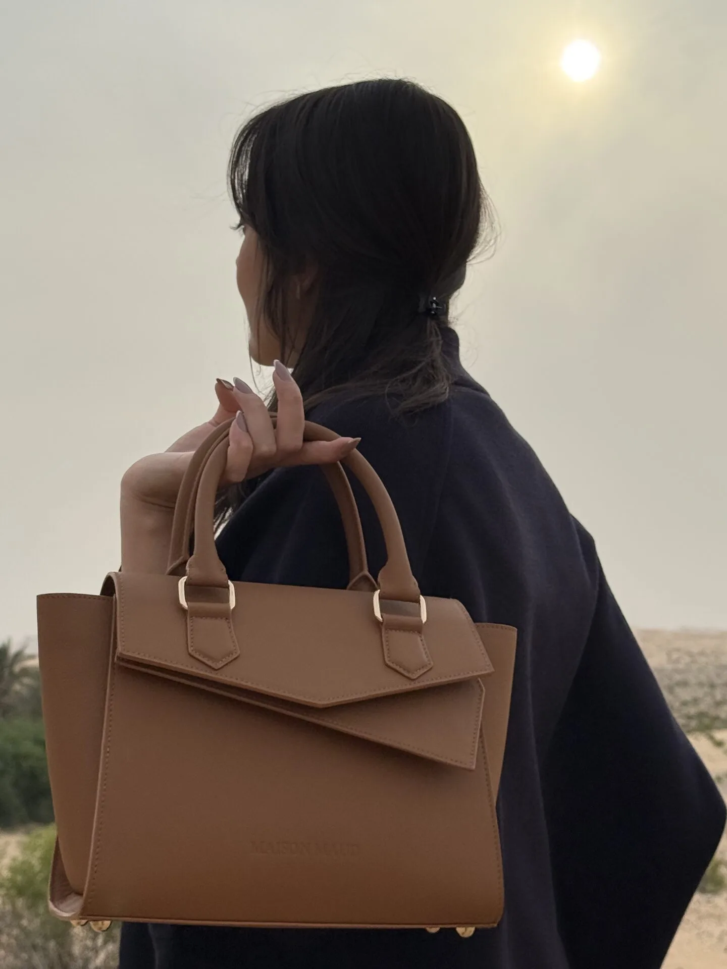 Woman carrying Handbag ÉdÉ over shoulder, desert sunset behind